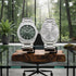 Two silver watches on a wooden stand with a forest view in the background